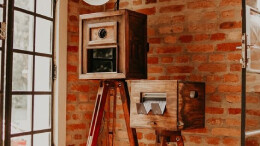 A camera on top of a tripod in front of a brick wall.